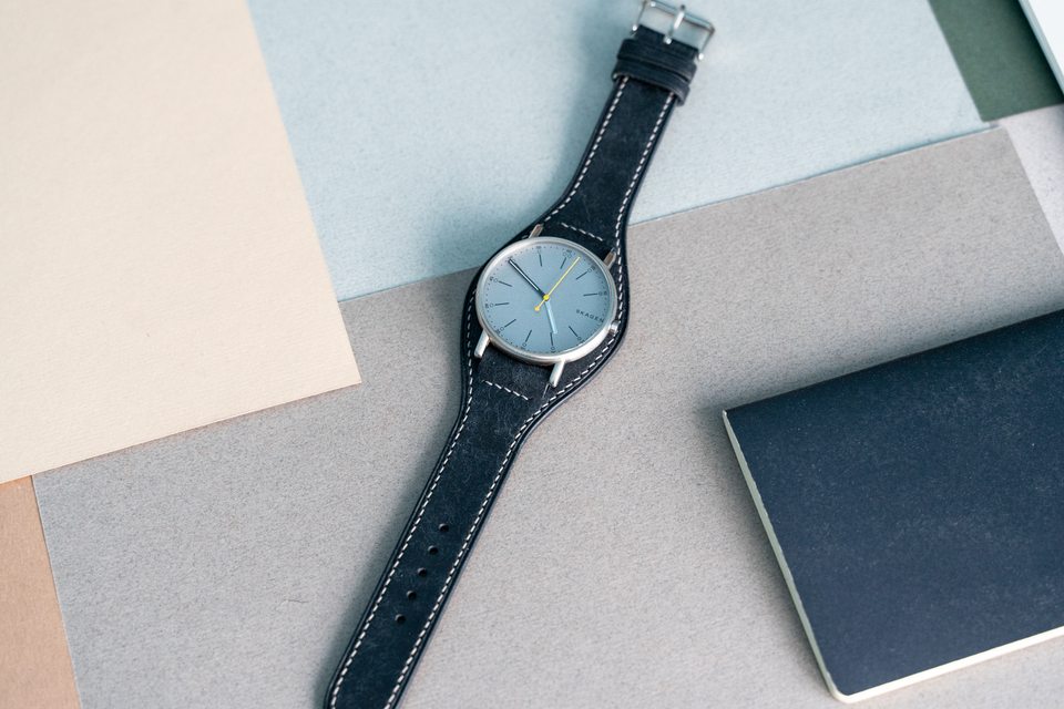 Black Bund strap and pale-dial watch laid flat beside a notebook.