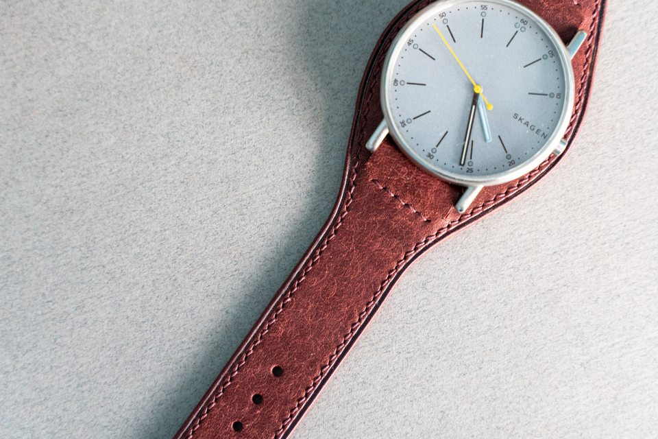 Close view of red leather and light stitching beside the round watch case.