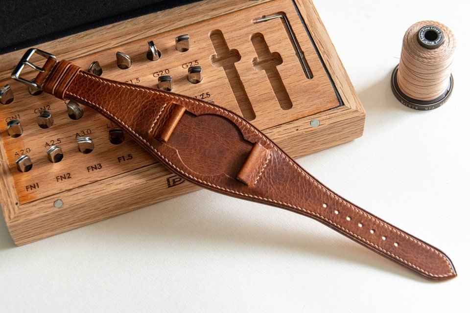 Textured cognac Bund strap laid across a wooden tool box beside a spool of light thread.